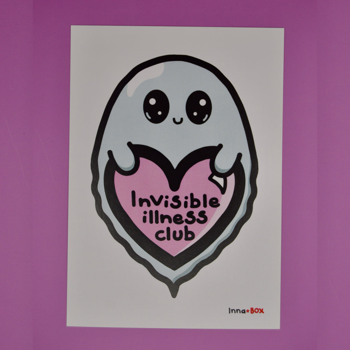 A white rectangular postcard featuring a cute ghost character with large eyes holding a pink heart that reads 'Invisible illness club,' shown against a solid purple background. A small 'InnaBox' logo appears at the bottom right of the print.