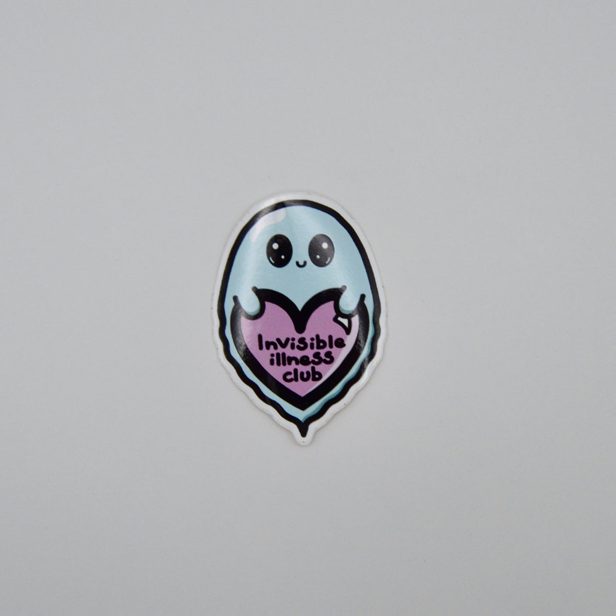 A sticker featuring a cute light blue ghost character holding a pink heart that reads 'Invisible illness club' in black text, shown on a plain light gray background.