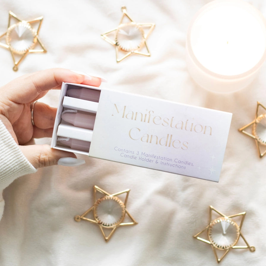 Hand holding a box of 'Manifestation Candles' with star-shaped candle holders on a soft surface.