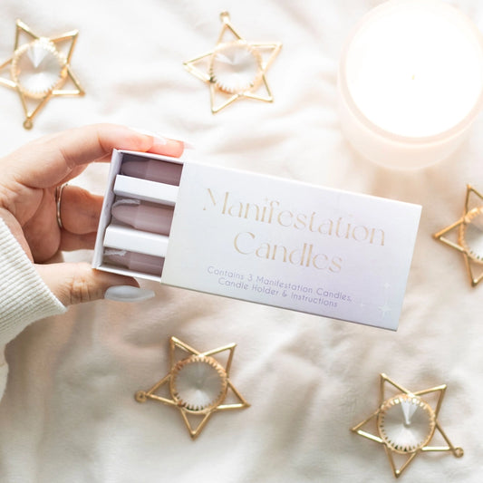 Hand holding a box of 'Manifestation Candles' with star-shaped candle holders on a soft surface.