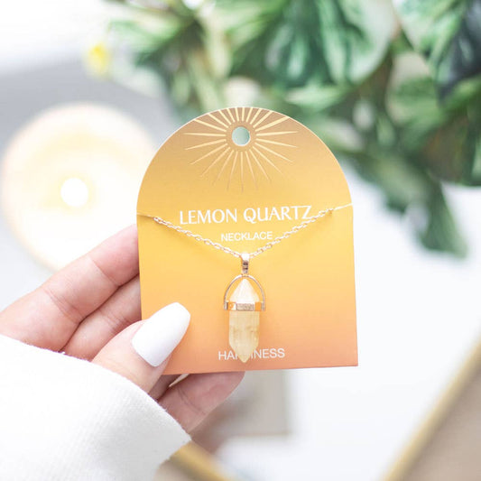 Hand holding a lemon quartz necklace on a branded card with a blurred green plant background