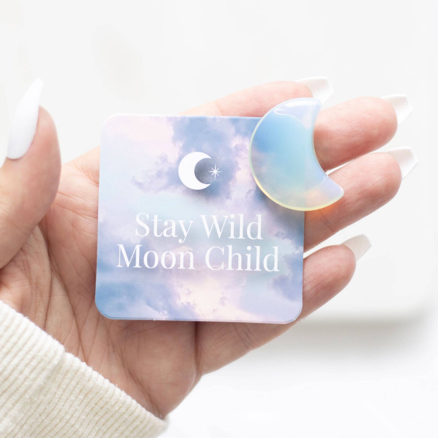 Hand holding a card with 'Stay Wild Moon Child' text and a moon shaped crystal.