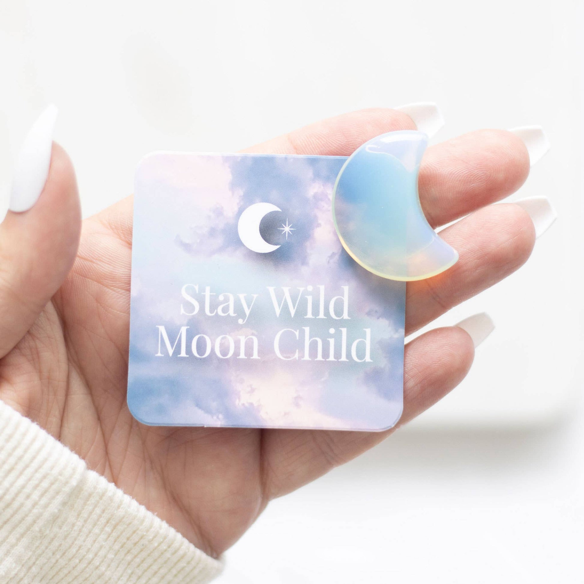 Hand holding a card with 'Stay Wild Moon Child' text and a moon shaped crystal.
