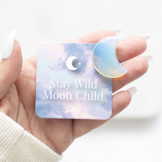 Hand holding a card with 'Stay Wild Moon Child' text and a moon shaped crystal.