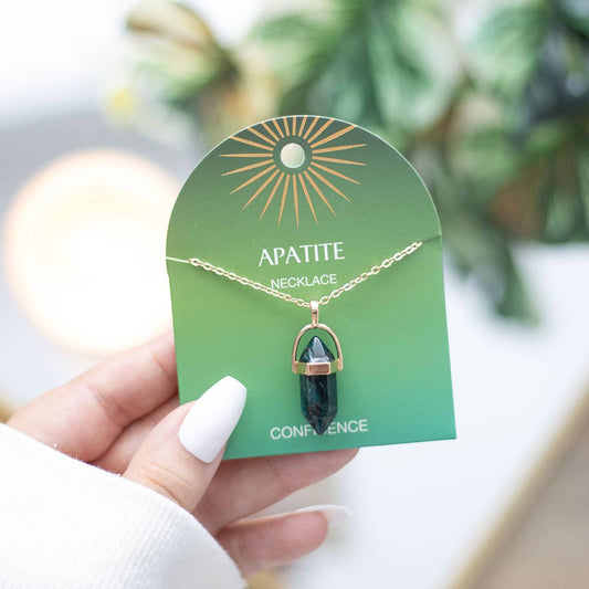 Hand holding a green apatite necklace on a green card with a blurred plant background