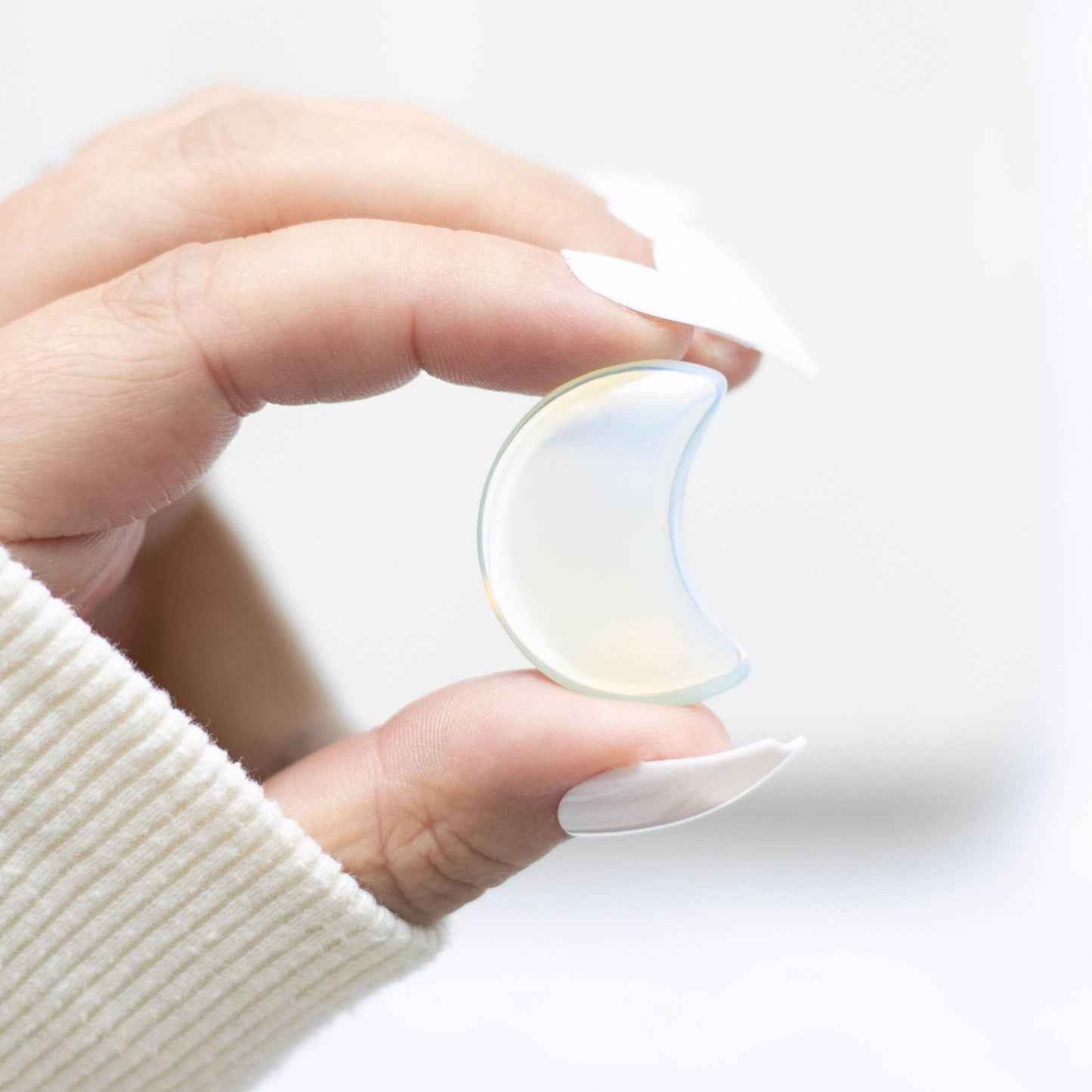 Hand holding a semi-translucent moon-shaped crystal against a white background