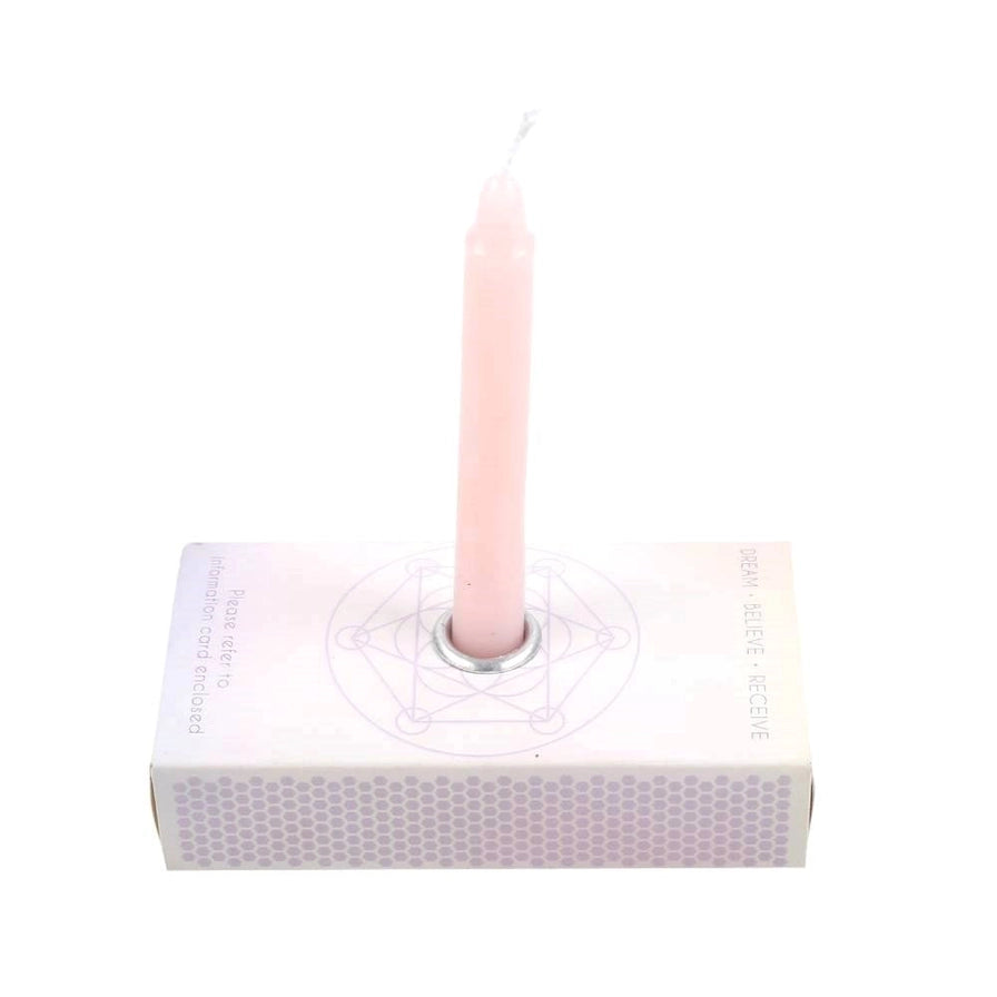 A pale pink taper candle standing upright in a square white box with a geometric line drawing on the lid, photographed against a plain white background.
