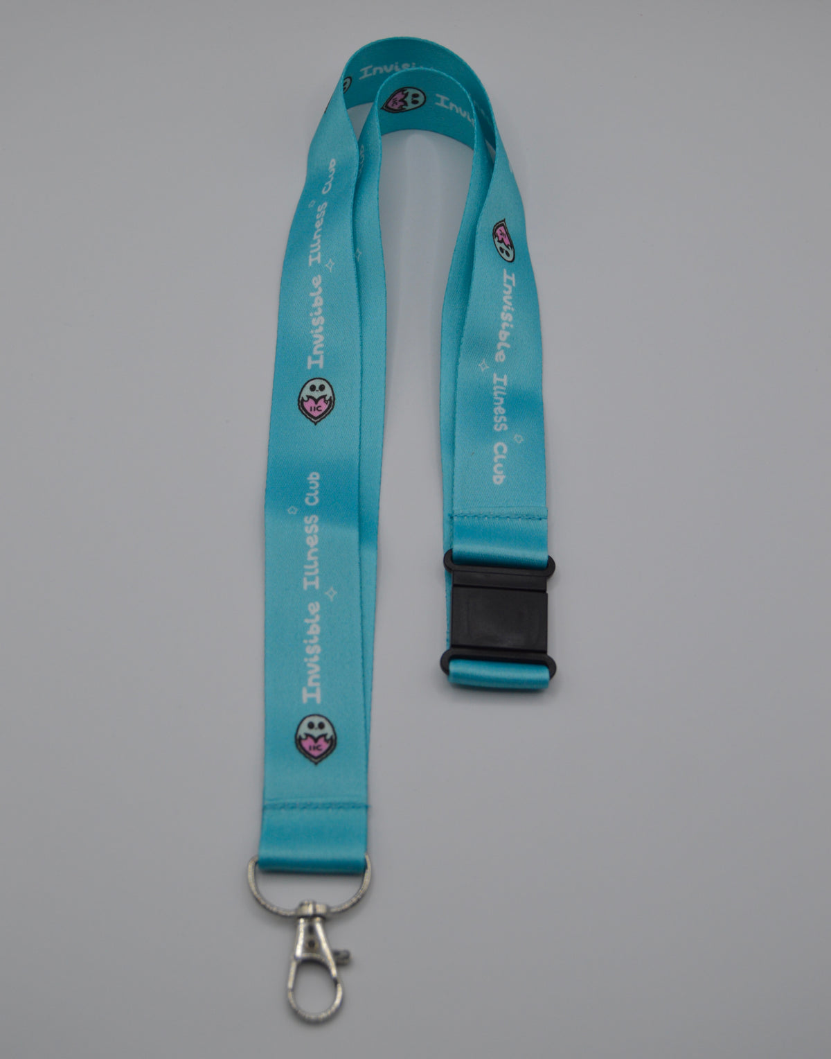 A turquoise-blue lanyard with a black plastic buckle and a silver metal clasp, featuring the text 'Invisible Illness Club' and a small ghost logo printed repeatedly on a neutral gray background.