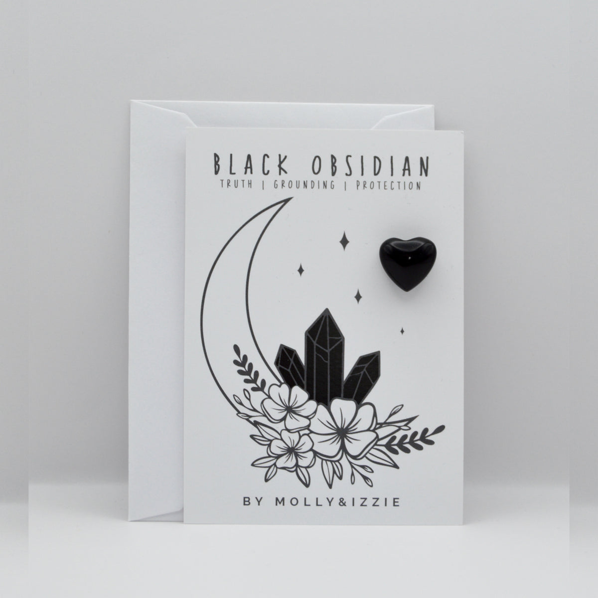 A white greeting card with black line art of a crescent moon, crystals, flowers, and stars, featuring the text 'BLACK OBSIDIAN' and 'Truth, Grounding, Protection', shown with a white envelope behind it on a light gray background.