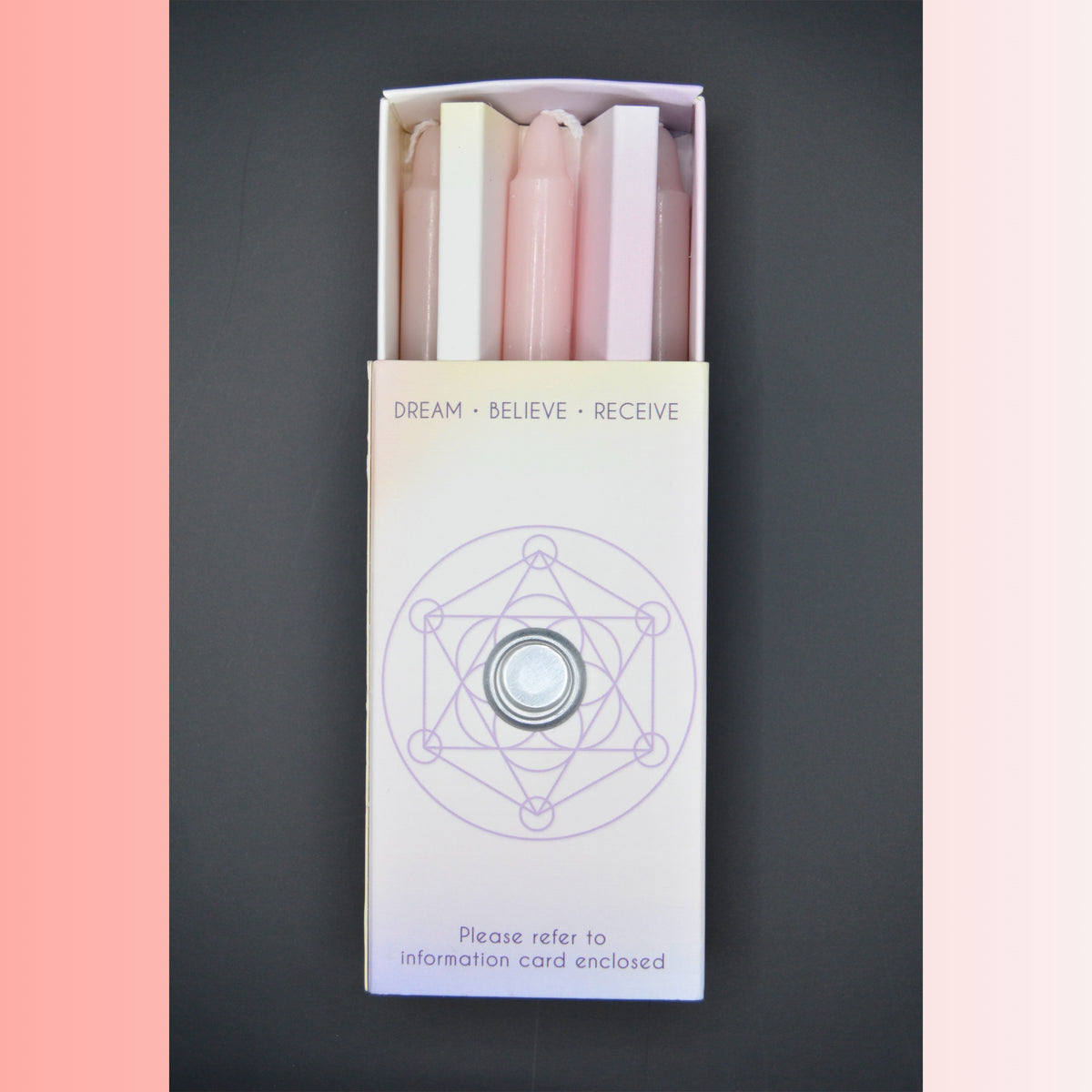 A boxed set of 3 pink pastel-colored candles in a white box with a purple geometric design and the text 'DREAM • BELIEVE • RECEIVE' on a dark gray background.