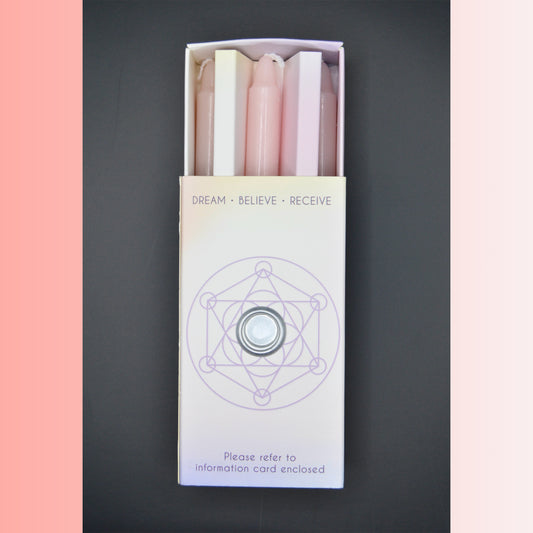 A boxed set of 3 pink pastel-colored candles in a white box with a purple geometric design and the text 'DREAM • BELIEVE • RECEIVE' on a dark gray background.