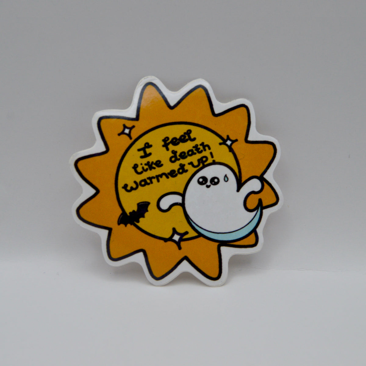 A yellow sun shaped sticker with a cartoon bat and ghost with text that reads 'I feel like death warmed up!'.
