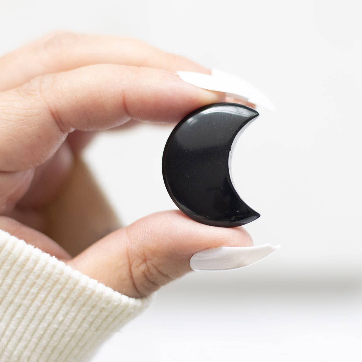 Hand holding a black crescent moon-shaped crystal against a white background